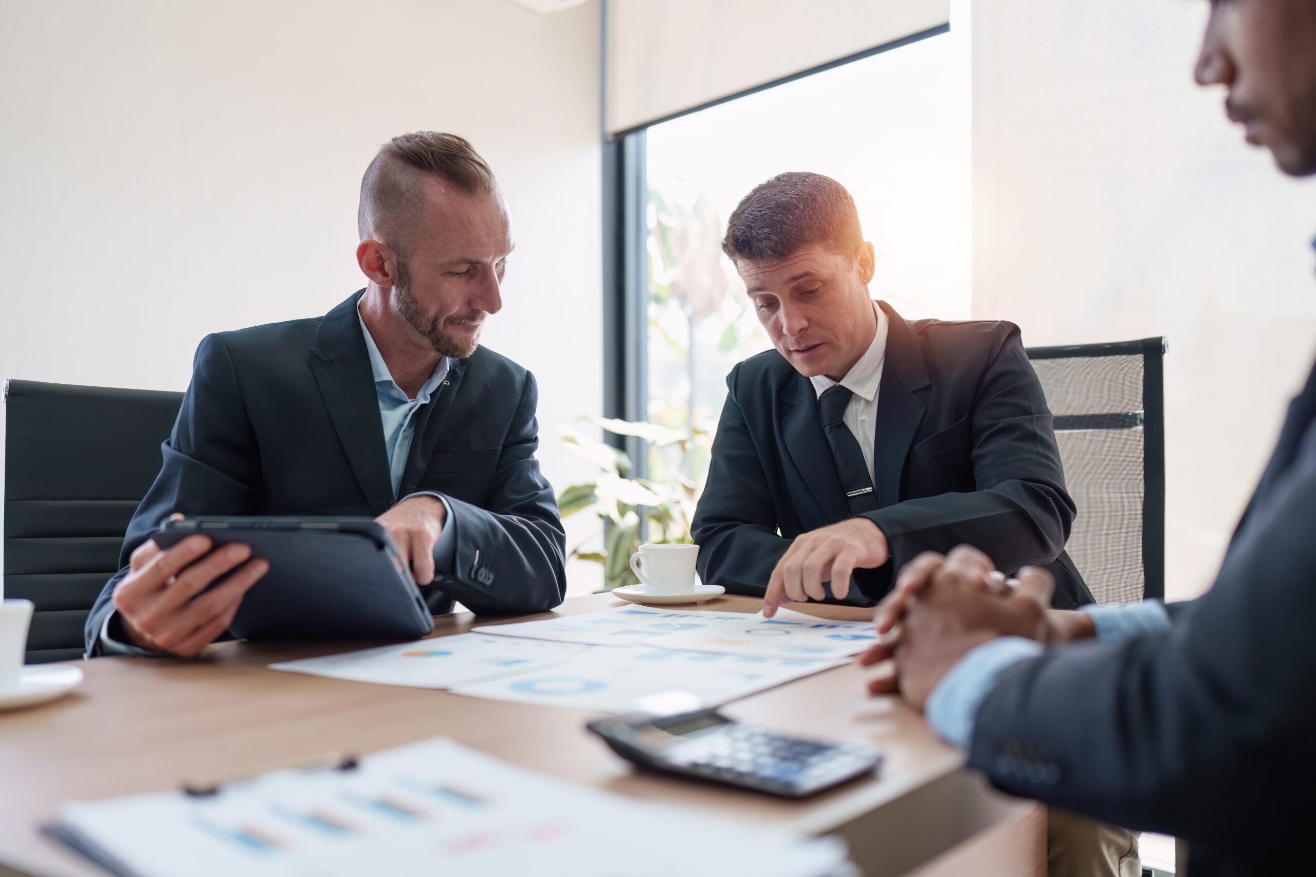 Group of Business financial with finance reports to analyze big data, balance sheet, strategy at meeting room. Business professionals in formal attire discussing charts and graphs of offshore trust setup at a meeting table, with a tablet and documents spread out in a bright office setting.